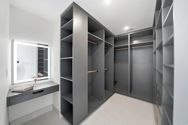 Custom closet system featuring extensive shelving, built-in drawer storage, multiple hanging rods, and a dedicated vanity area with an illuminated mirror