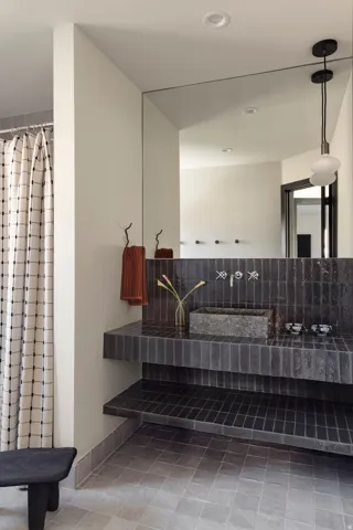 Full-height mirror, stone vessel sink, wall-mounted faucet, and dark tile vanity