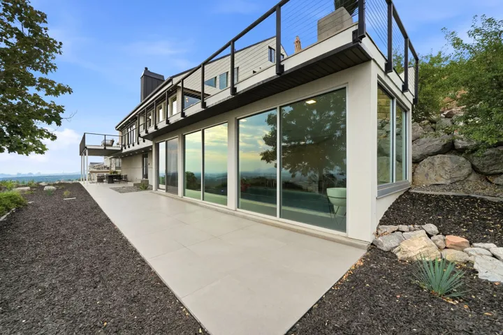 Exterior featuring expansive glass panels, a concrete patio, and a second-story balcony with cable railings