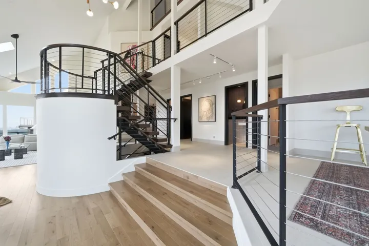 Hardwood flooring, curved staircase with cable railing, high vaulted ceilings, and upper level balcony