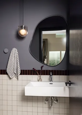 Wall-mounted sink with chrome faucet, black wall-mounted faucet, and abstract-shaped mirror