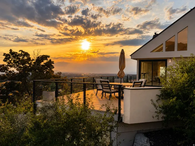 Expansive outdoor deck with cable railing, city backdrop, and large sliding glass door entry
