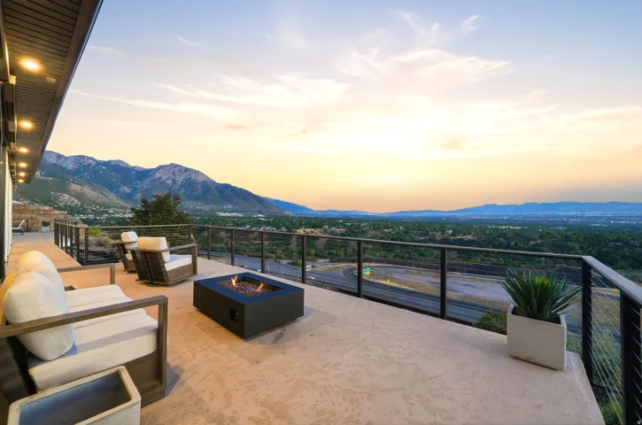 Expansive outdoor patio with a built-in fire pit, glass and metal railing, and recessed soffit lighting