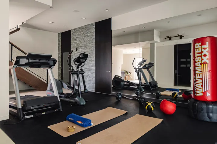 Dedicated fitness space featuring a full-width mirrored wall, durable rubber flooring, and recessed lighting