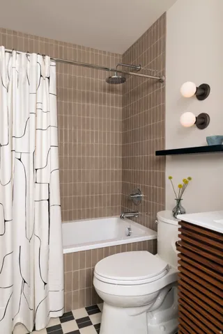 Subway tile shower surround, chrome shower fixture, checkerboard floor tile, wall-mounted vanity with wood-finish slatted front, and dual wall sconces
