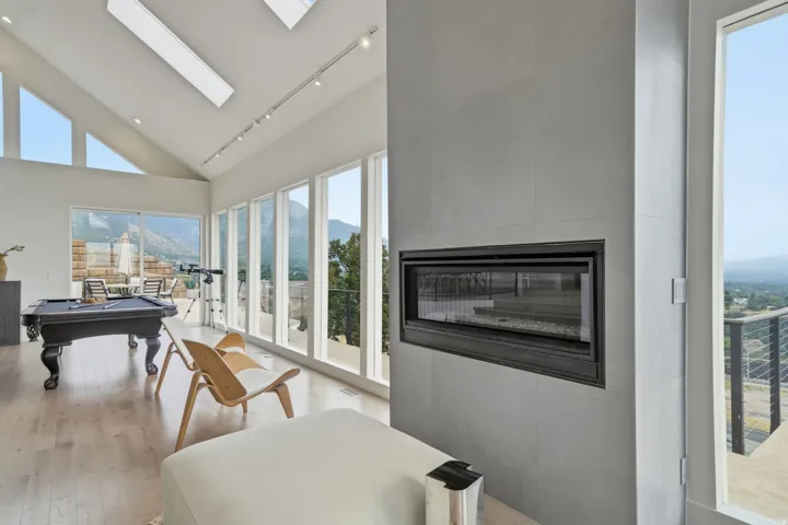 Vaulted ceiling with skylights, linear fireplace set in a tiled wall, light wood-finish flooring, and multiple floor-to-ceiling windows