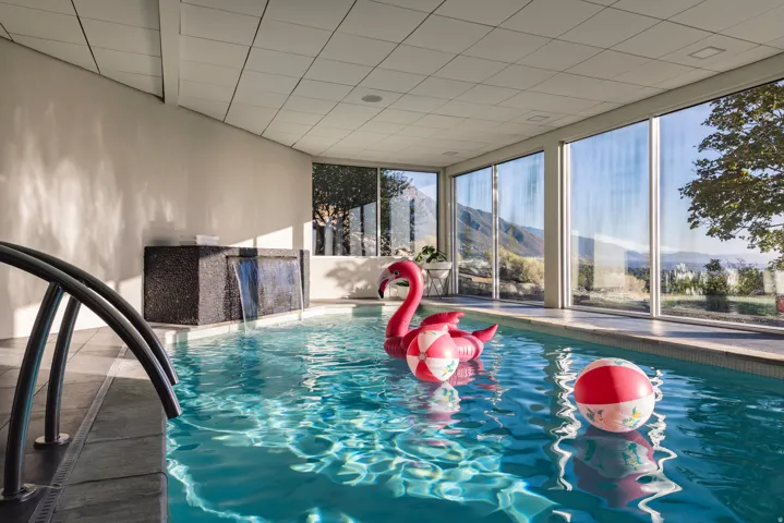 Indoor swimming pool with full-height windows, a textured accent wall, and an integrated waterfall feature