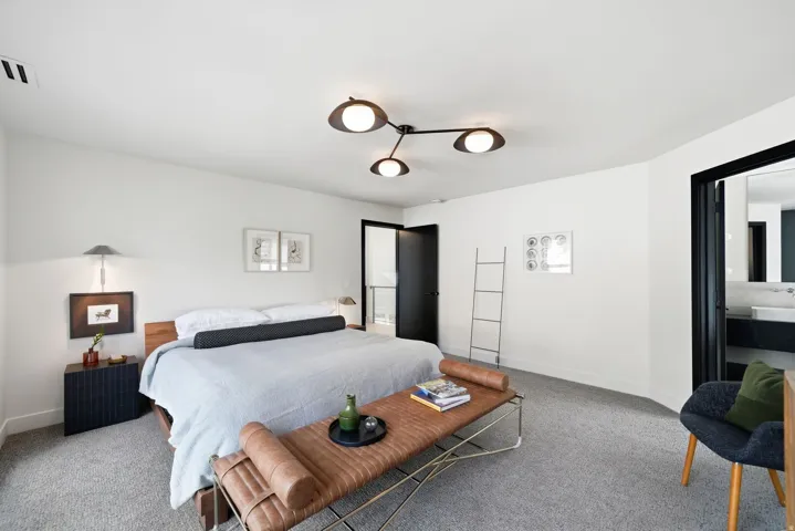 White walls, gray carpet, black ceiling fan with three lights, dark wood-finish headboard, and a black door frame