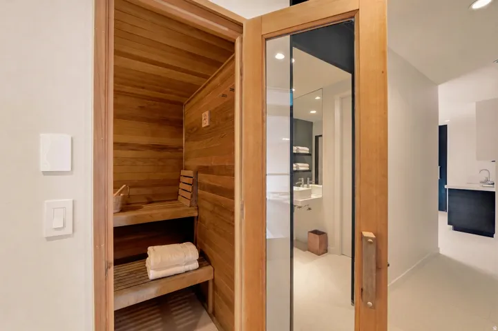 Wood-paneled sauna with built-in wooden benches and an adjacent room featuring a wall-mounted sink