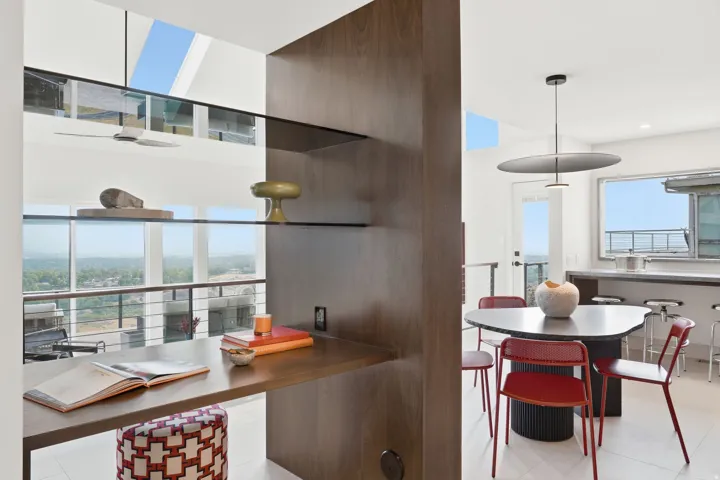 Integrated wood-finish shelving and desk, expansive multi-level window system, sleek kitchen island with bar seating, and a modern pendant light fixture