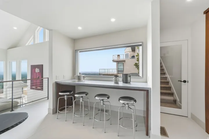 Built-in bar with a light-toned countertop and wood-finish cabinetry, recessed lighting, and a window framing the horizon