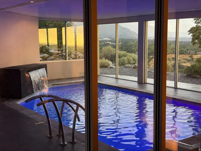 Indoor swimming pool featuring a waterfall, integrated lighting, and stainless steel grab bars