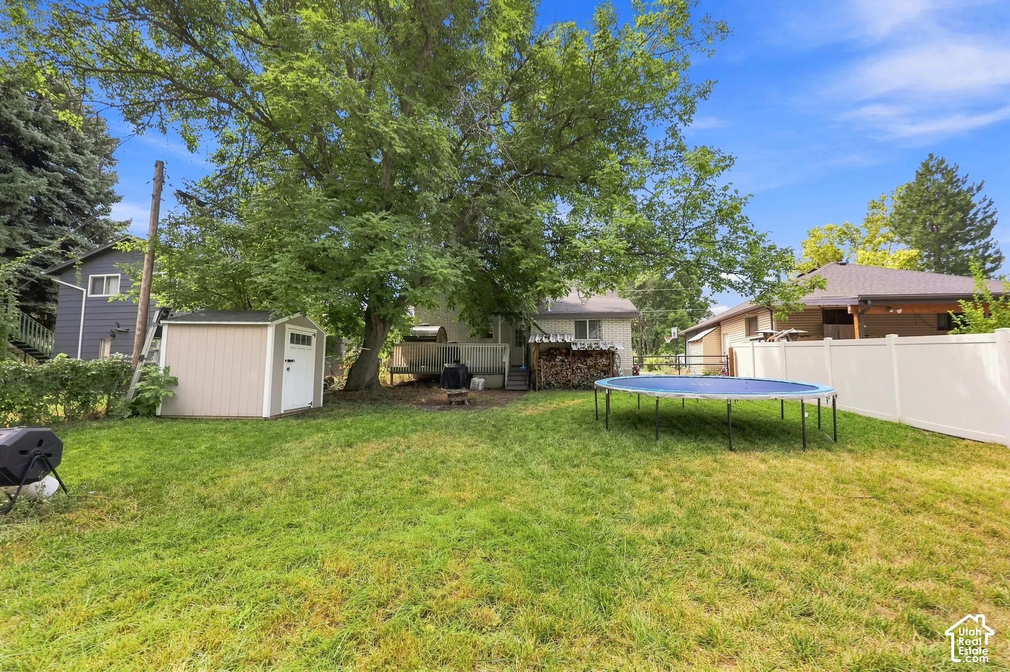 Expansive backyard featuring a manicured lawn, mature trees, a white vinyl fence, and a neutral-toned storage shed