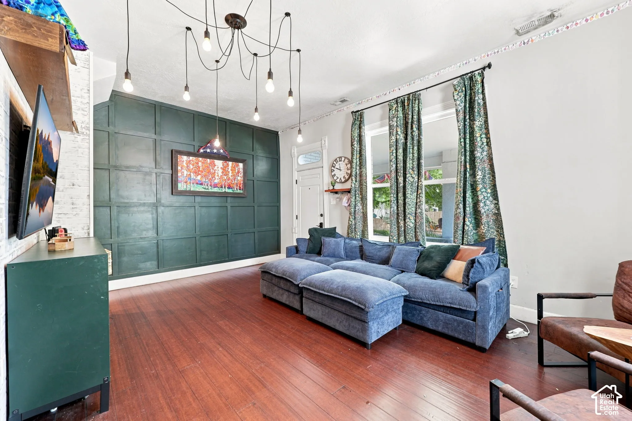 Dark wood-finish flooring, accent wall with paneled detailing, white brick wall texture, and multiple windows providing natural light