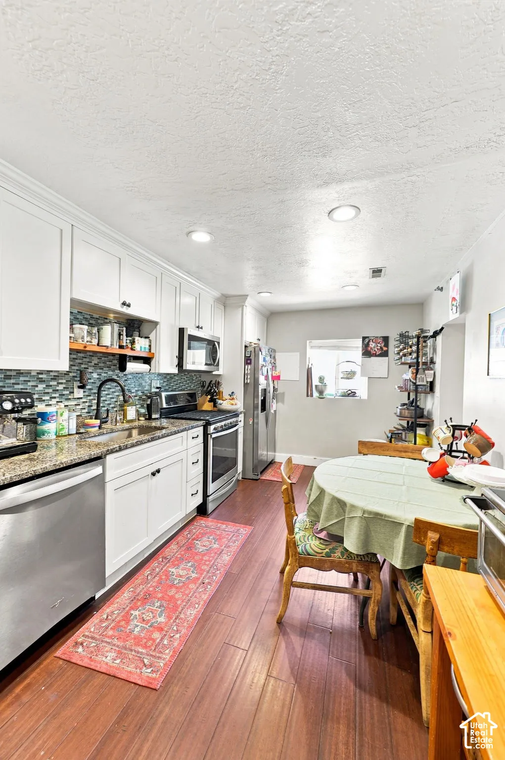 Kitchen featuring white cabinetry, wood-finish flooring, recessed lighting, stainless steel appliances, and a tiled backsplash