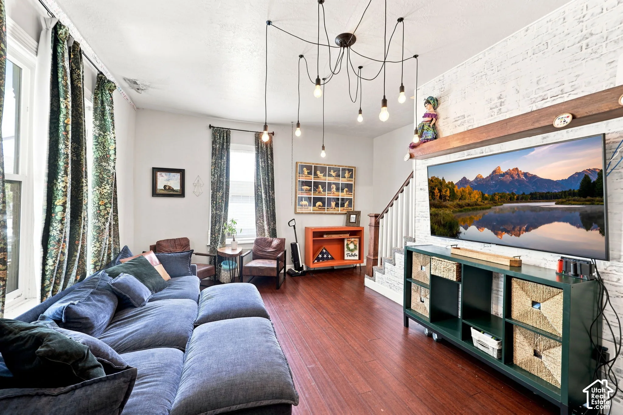 Hardwood-finish flooring, white painted brick accent wall, white staircase with wood railing, recessed windows, and a multi-bulb ceiling fixture