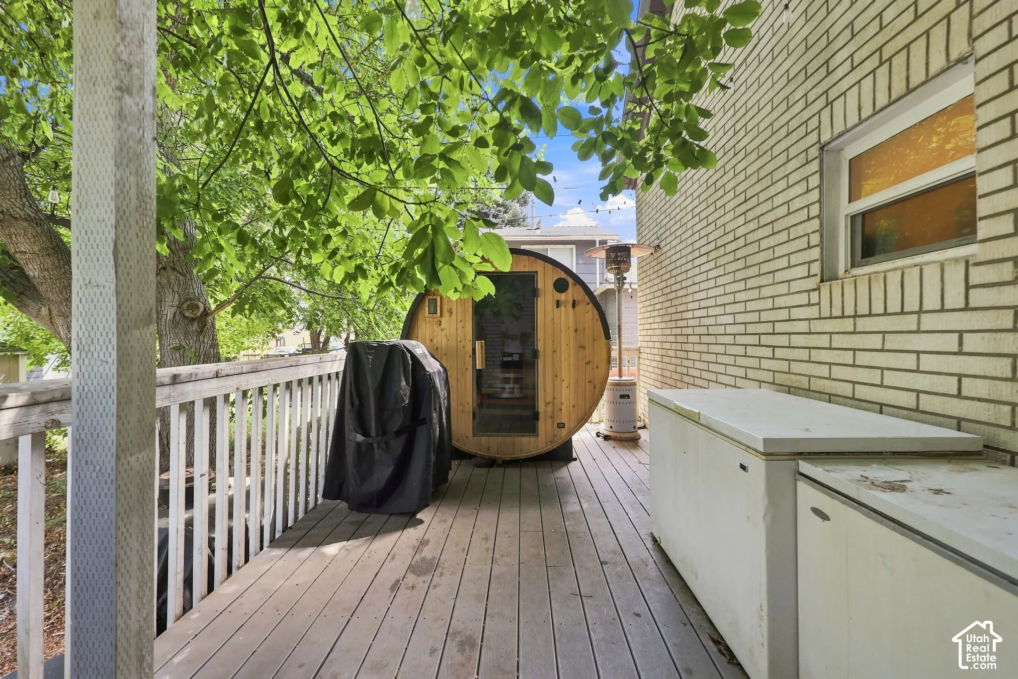 Expansive outdoor deck with a barrel sauna, wood railings, and brick exterior