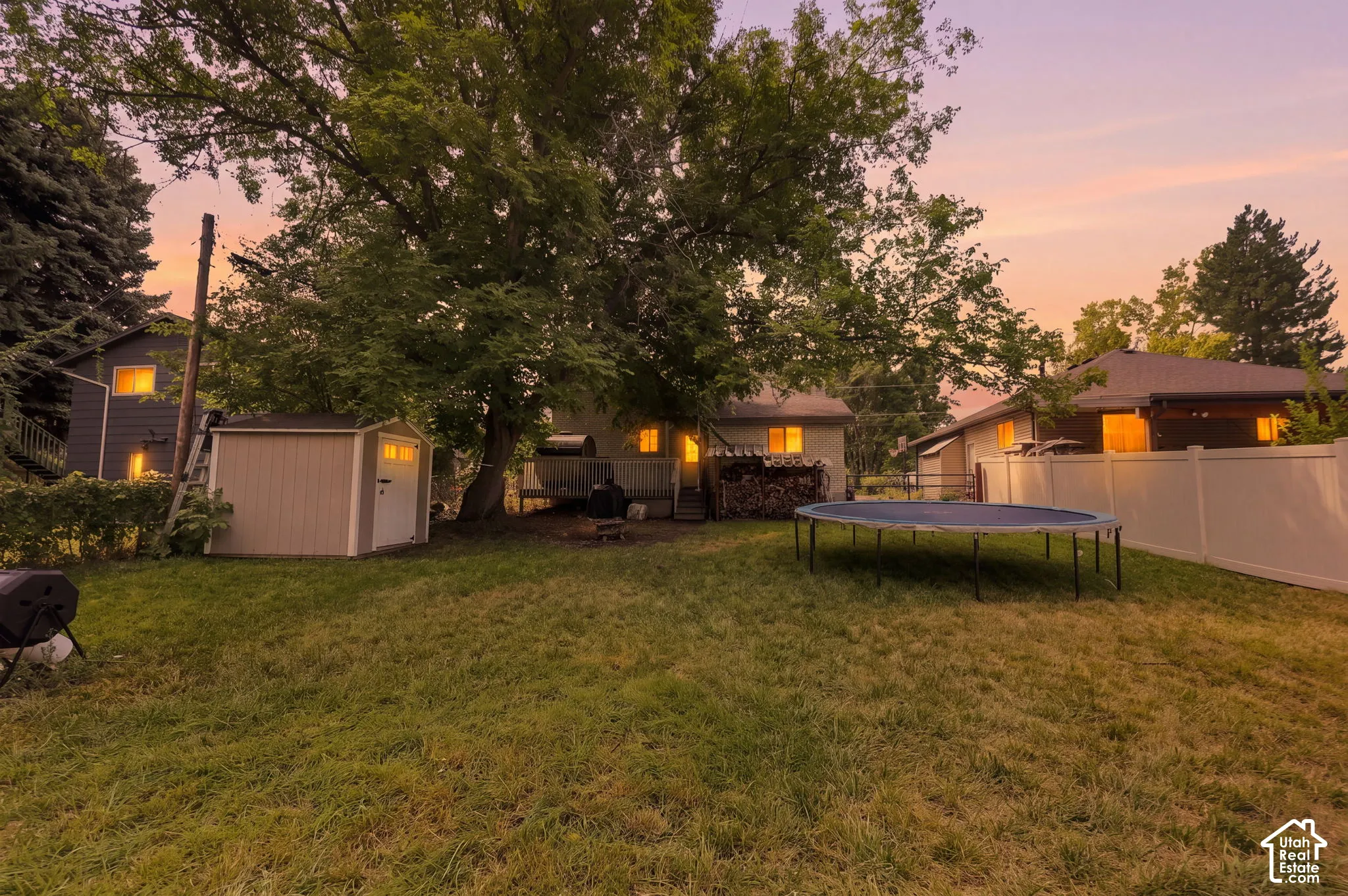 Expansive backyard featuring a lush lawn, mature trees, a permanent storage shed, and a white privacy fence