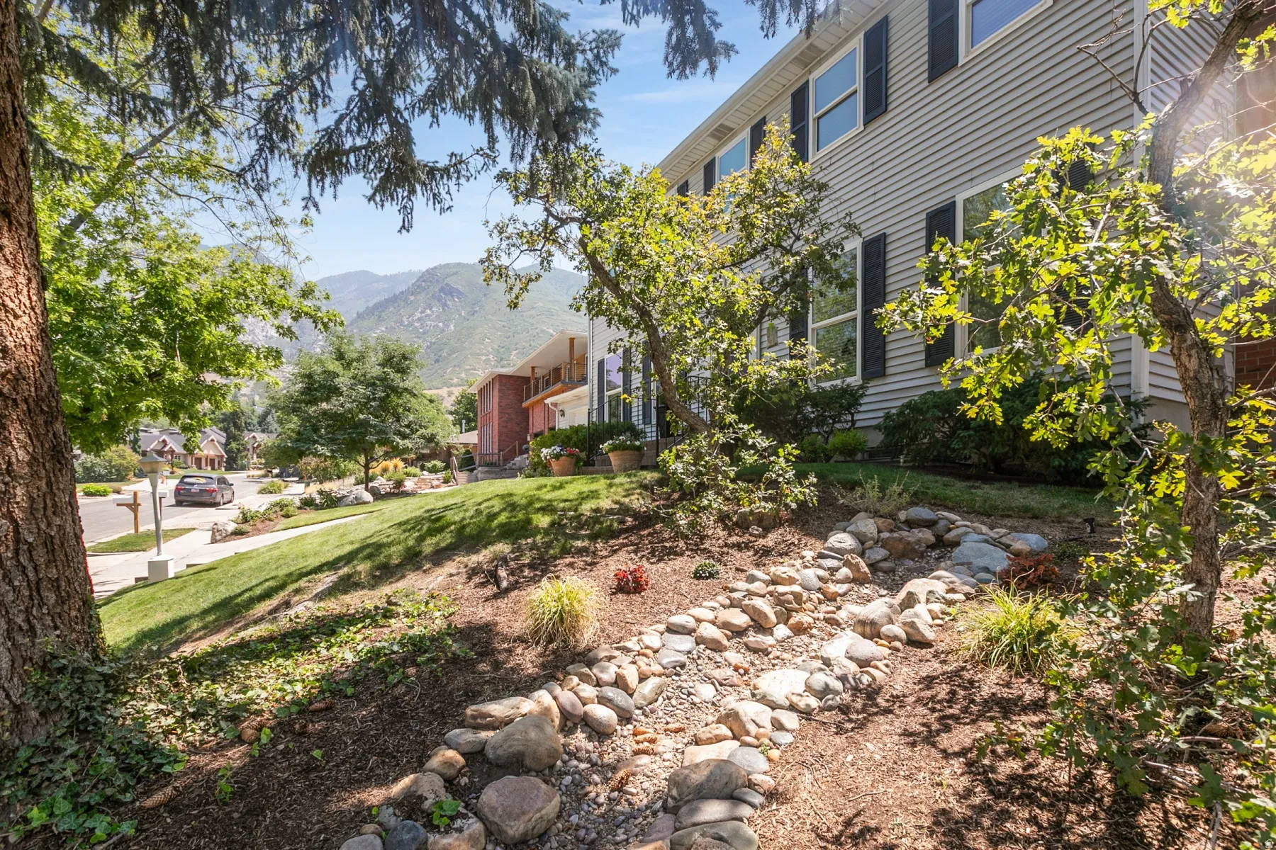Mature landscaping with a rock-lined dry creek bed, sloped lawn, and mountain scenery