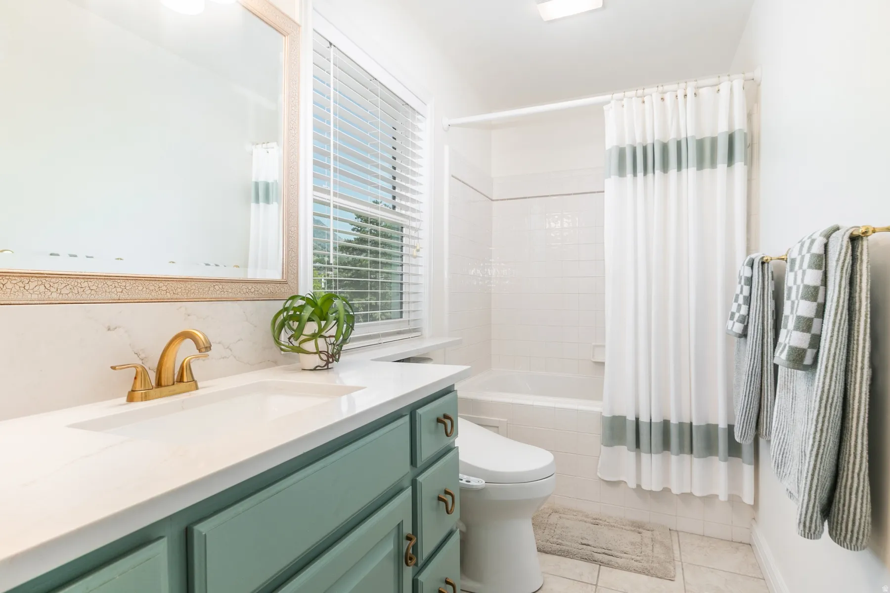 White-tiled bathroom featuring a mint green vanity with gold-tone hardware, a white countertop, and a built-in bathtub with subway tile surround
