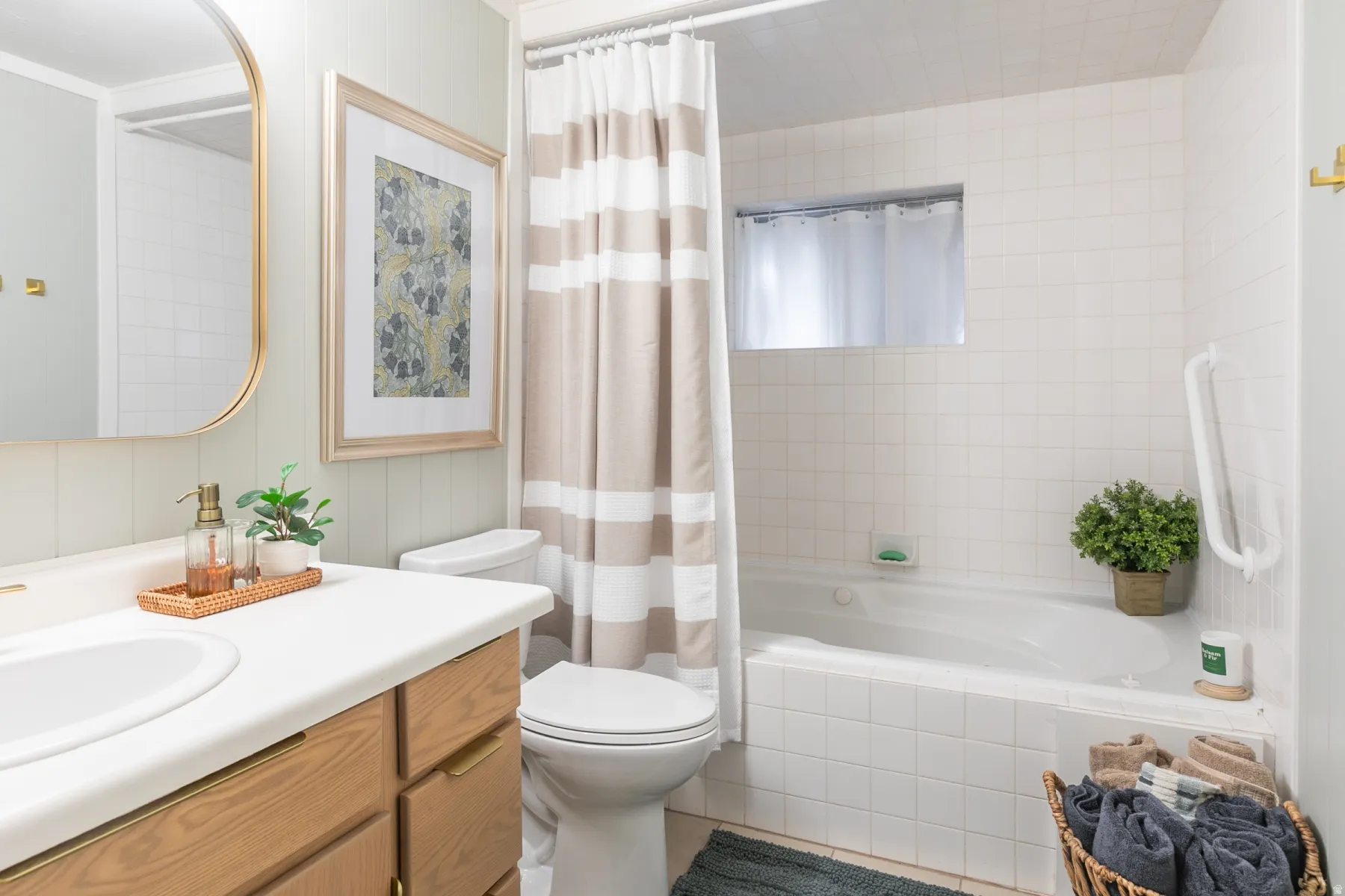 Built-in bathtub with white tile surround, wood-finish vanity with countertop and integrated sink, wall-mounted mirror with gold-tone frame