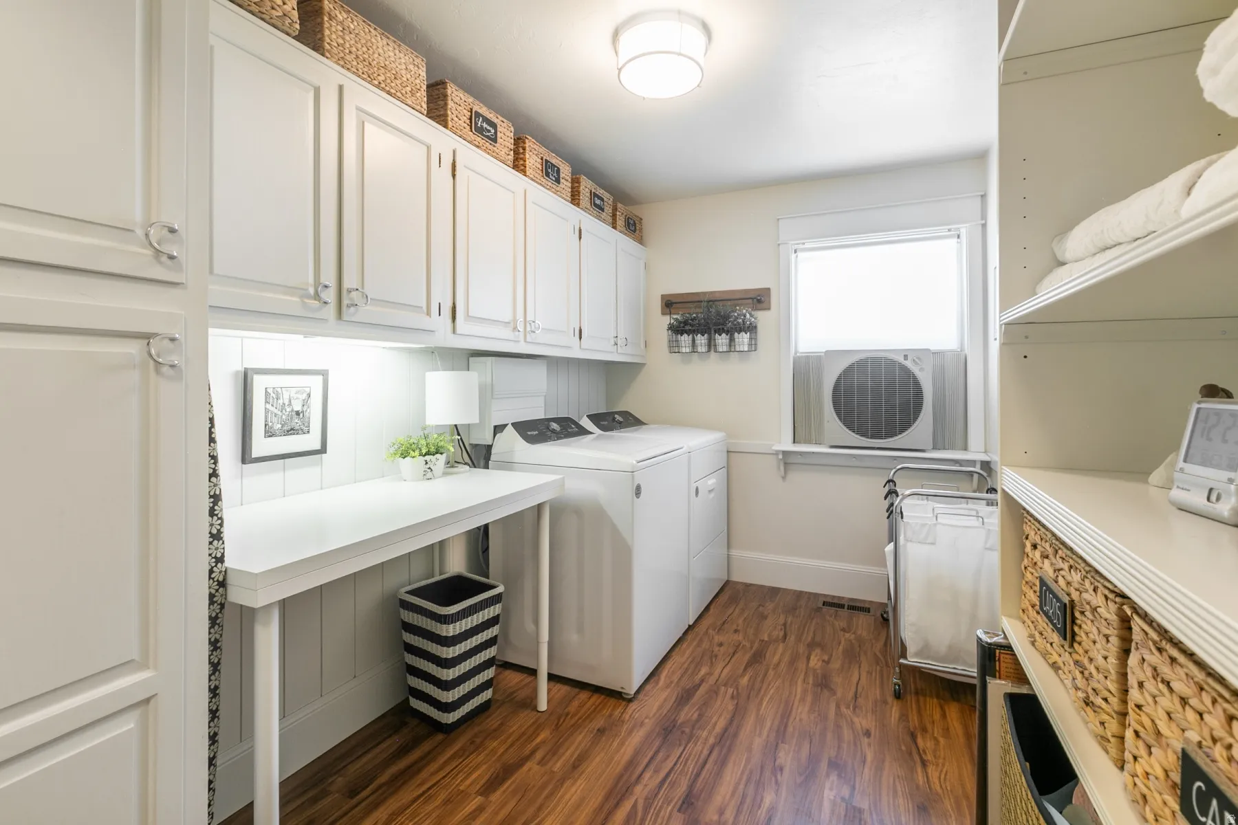 White cabinetry with silver-toned hardware, wood-finish flooring, built-in shelving, and a dedicated workspace