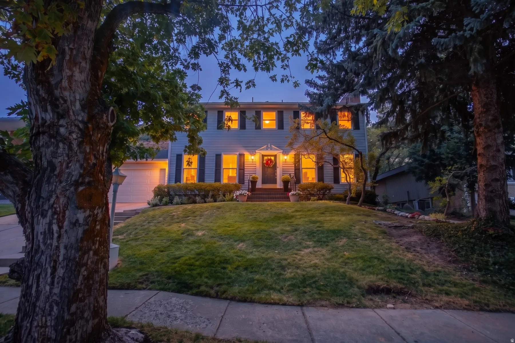 Two-story residence featuring a front entry with sidelights, a two-car garage, and mature landscaping