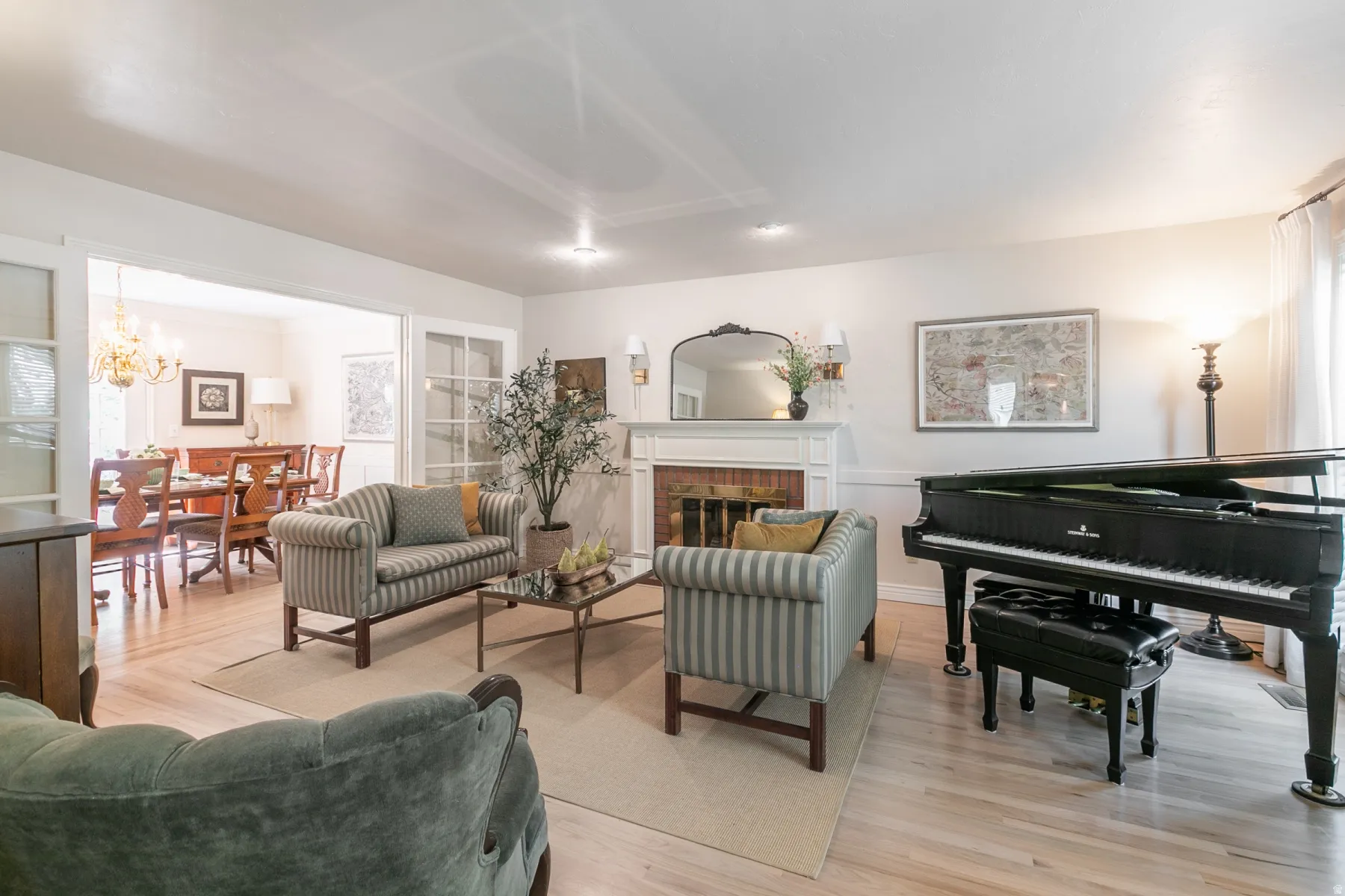 Elegant living room showcasing hardwood flooring, a fireplace with white surround and mantel, striped upholstered accent chairs, recessed ceiling lighting, and a grand piano