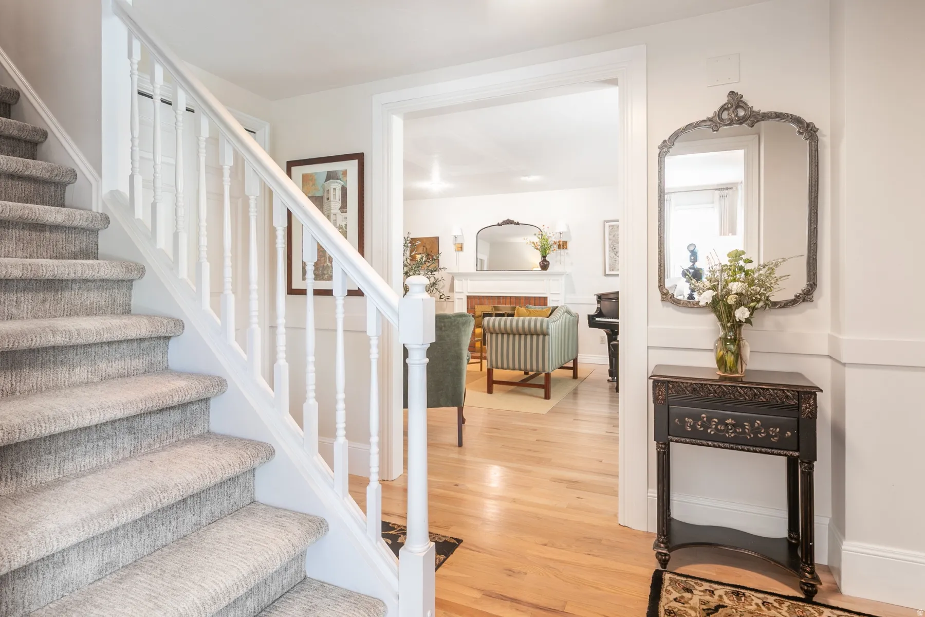 Carpeted staircase with white balusters and handrail, hardwood flooring, and a wide entryway leading to an interior space