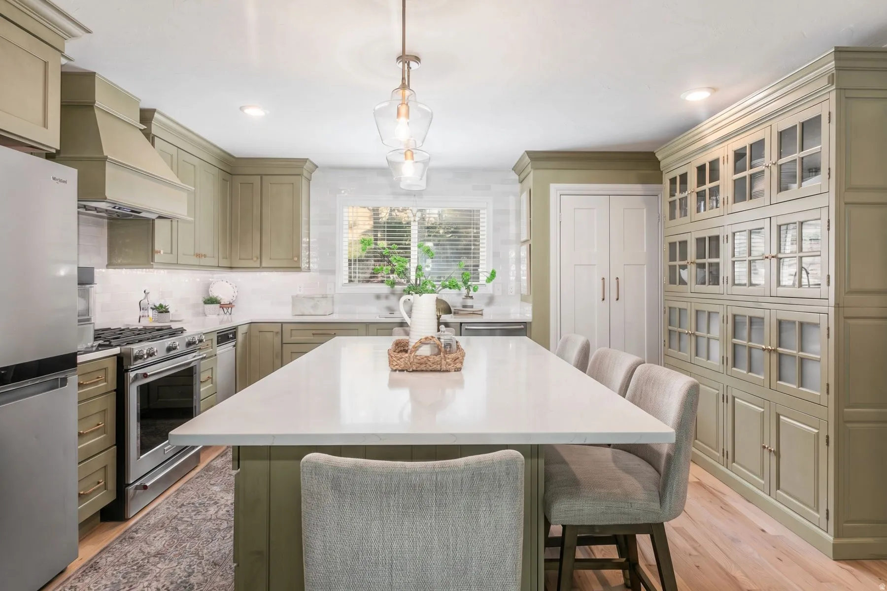 Kitchen featuring a large center island with seating, extensive cabinetry with glass-front uppers, stainless steel appliances, a white tile backsplash, and wood-finish flooring