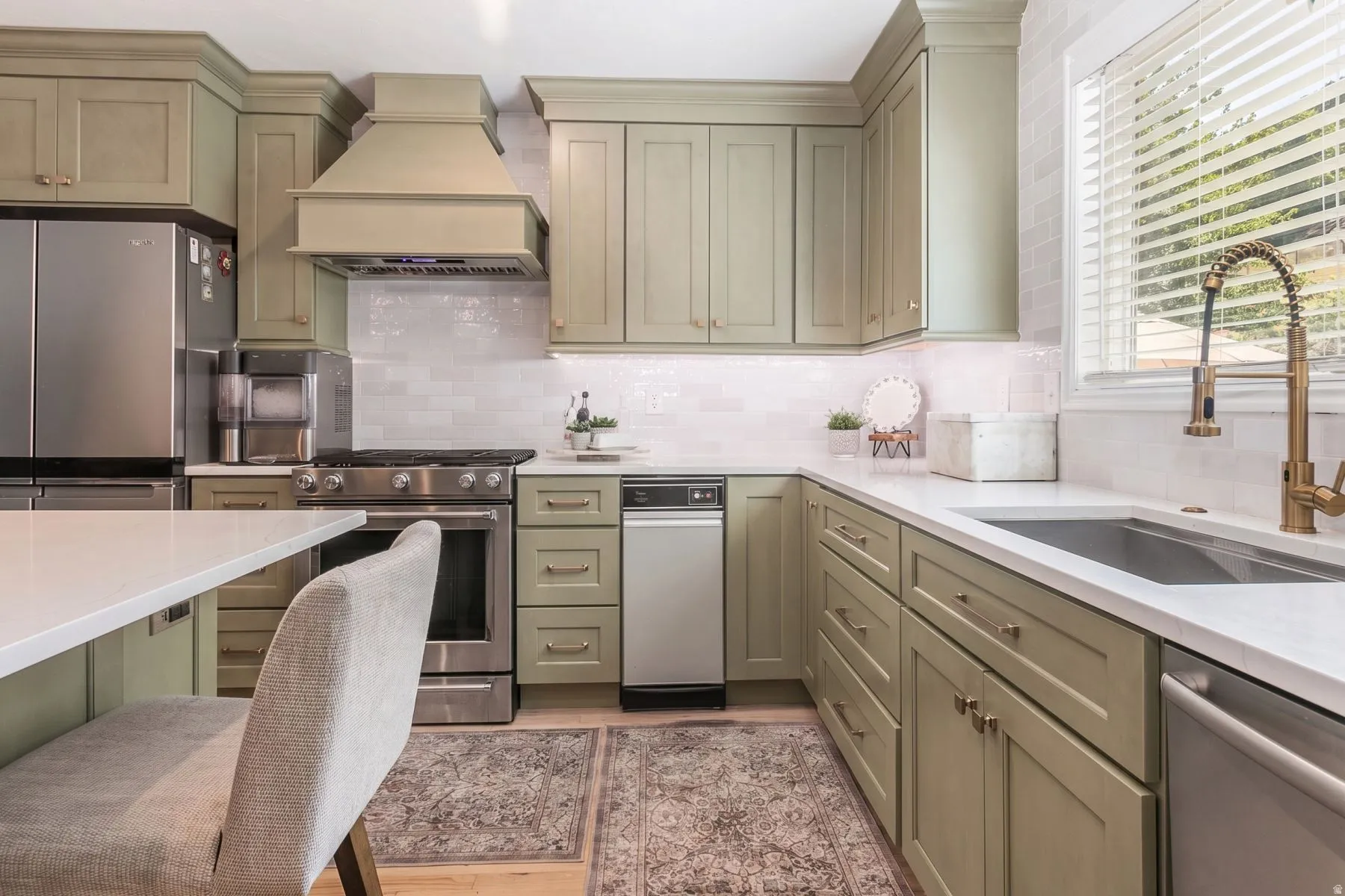 Elegant kitchen featuring soft-finish cabinetry, stainless steel appliances including a built-in dishwasher and range hood, white subway tile backsplash, and quartz countertops