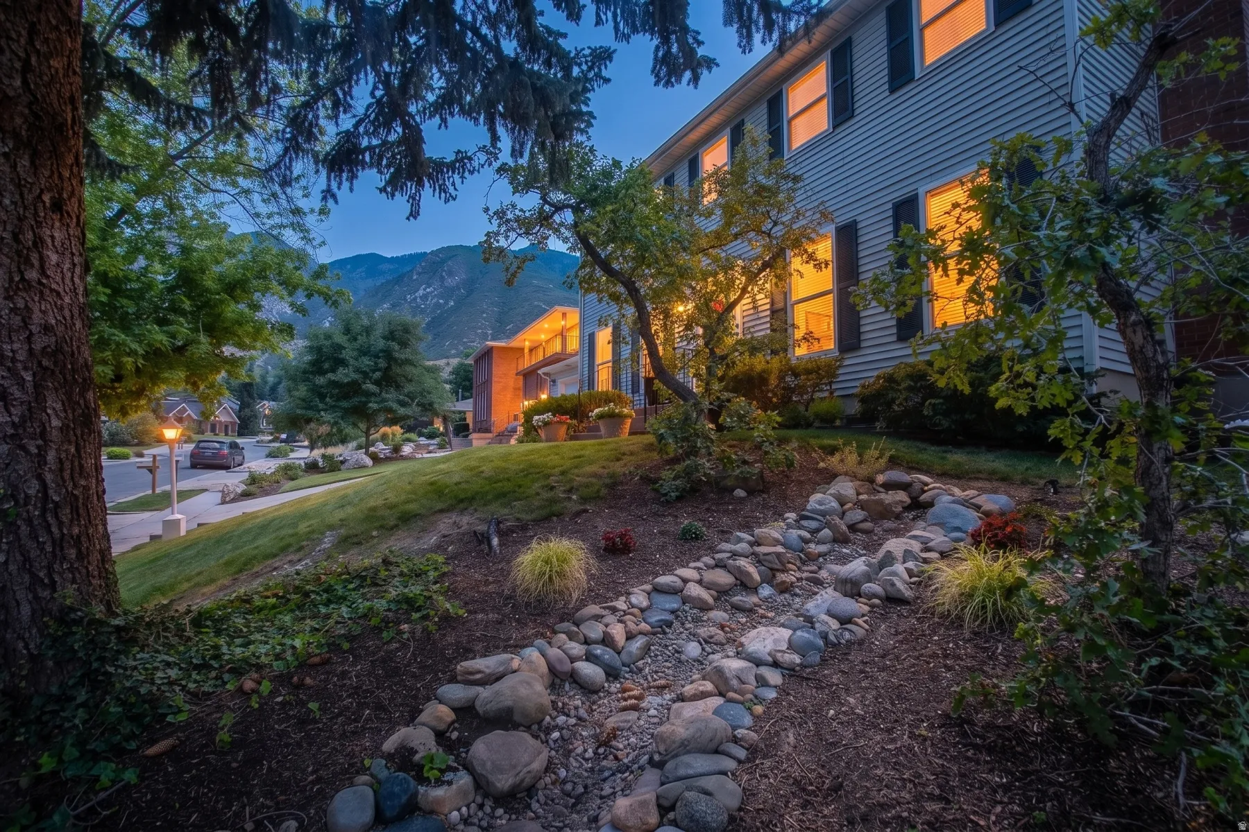 Exterior featuring vinyl siding, black window shutters, and a sloped, landscaped yard with decorative rocks