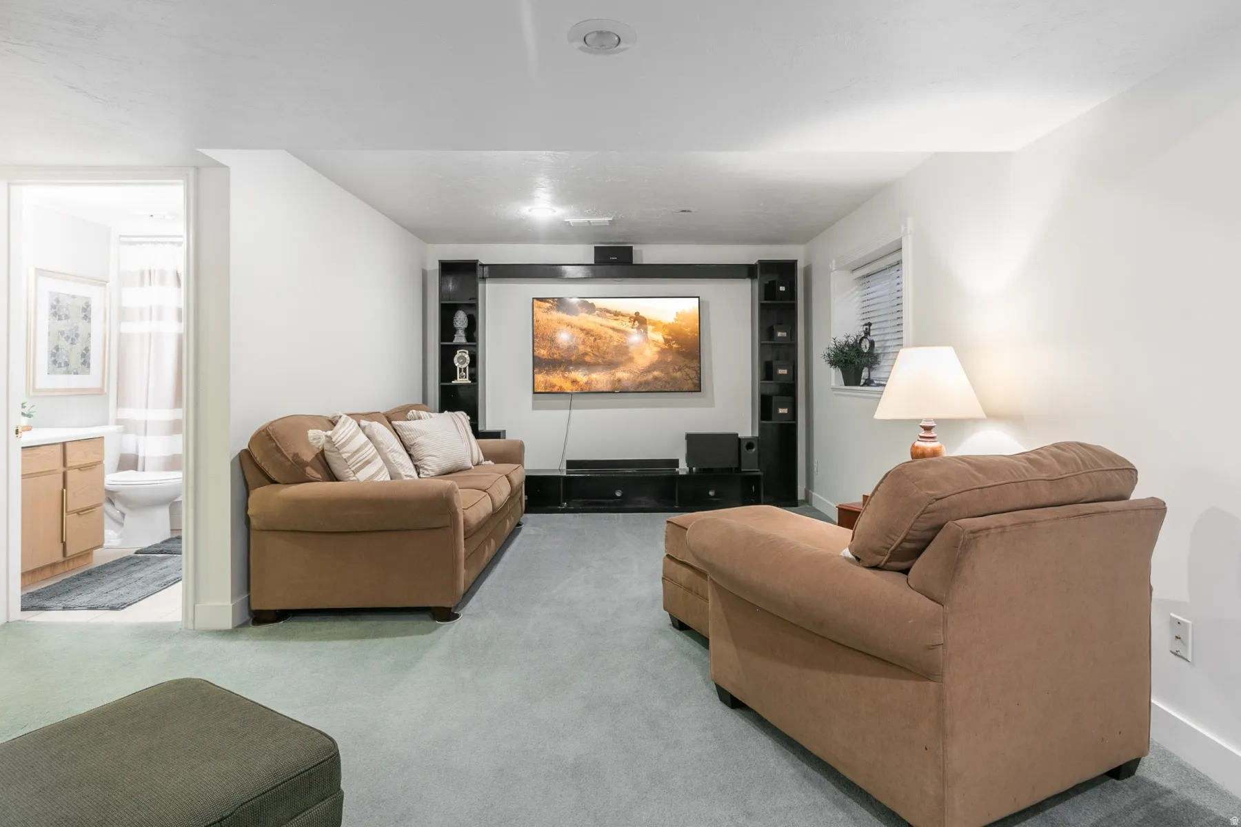Finished basement recreation room featuring a wall-mounted flat-screen television with built-in media cabinetry, recessed ceiling lighting, neutral carpet flooring, and ample seating arrangements