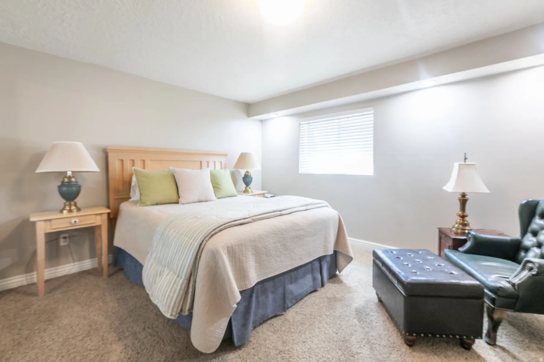 Spacious bedroom featuring a wood-finish headboard, carpet flooring, recessed ceiling lighting, and dual nightstands with table lamps