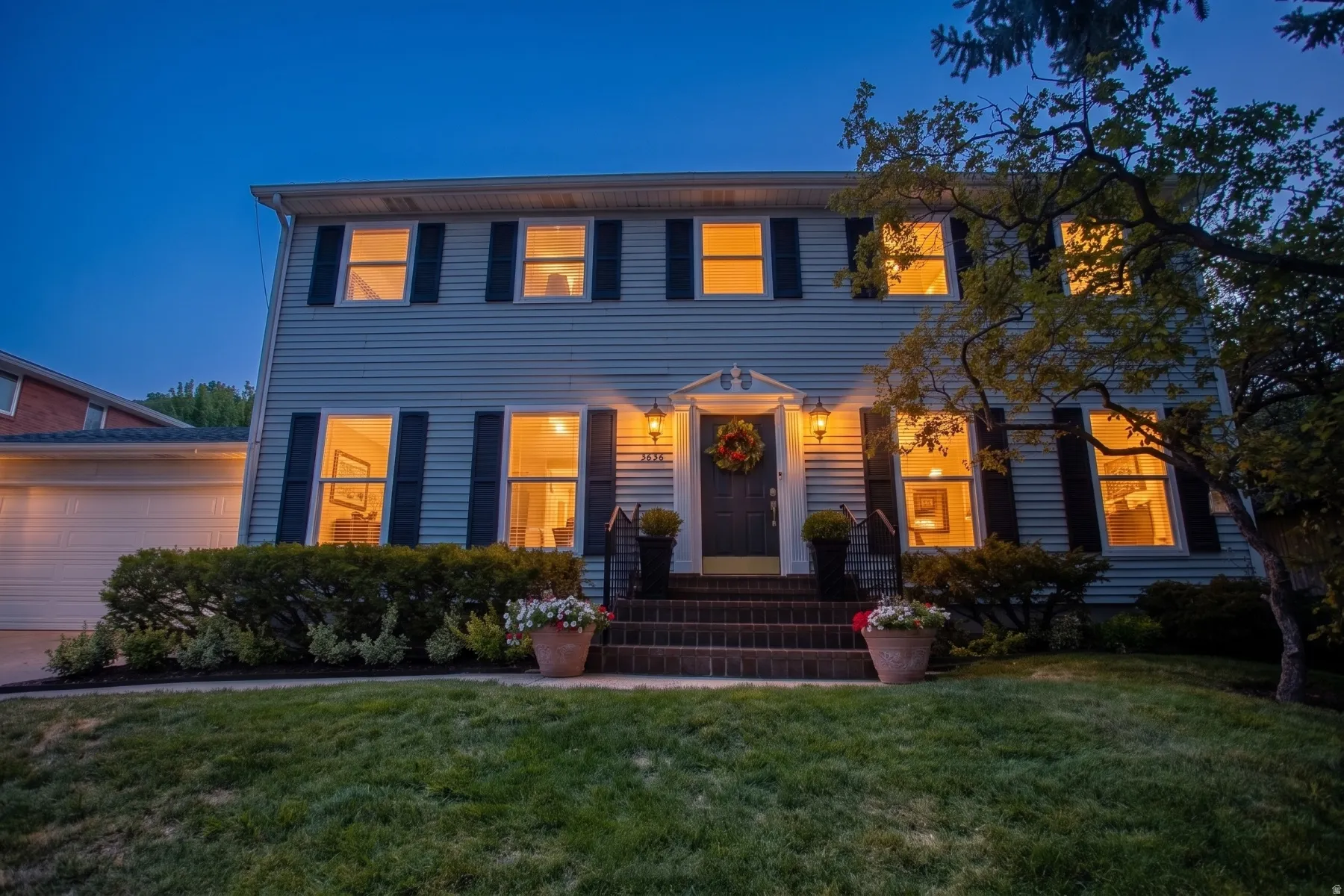 Two-story residence featuring siding exterior, an attached garage, brick steps, and exterior lighting