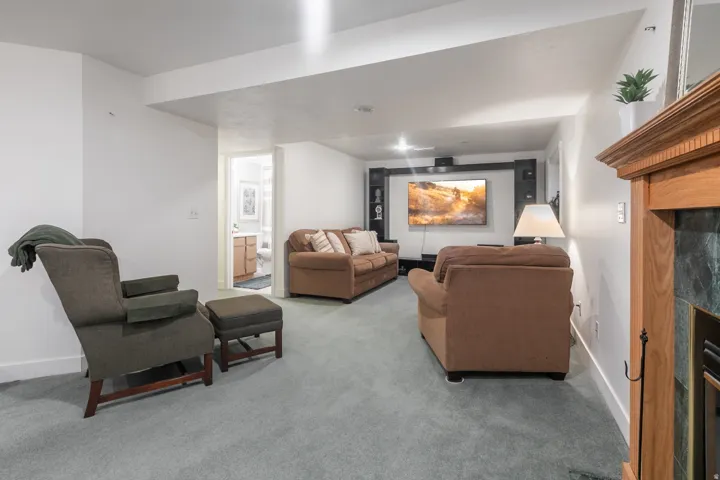 Finished basement recreation room featuring neutral carpet flooring, recessed ceiling lighting, a wood-burning fireplace with wood mantel, and wall-mounted flat-screen television