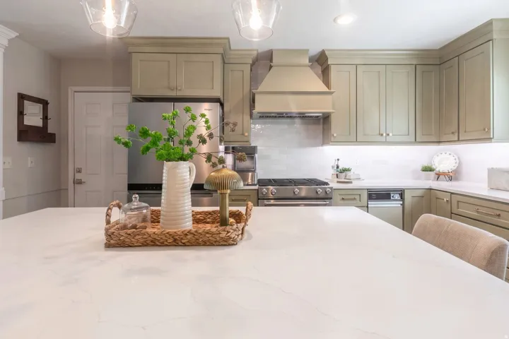 Elegant kitchen showcasing custom cabinetry with soft neutral finishes, a large quartz-topped island with seating, stainless steel gas range with overhead hood, white subway tile backsplash, and recessed lighting throughout