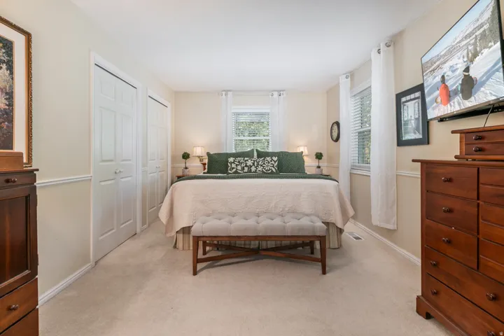 Spacious primary bedroom with neutral carpeting, abundant natural light from multiple windows, and wood-finish dressers