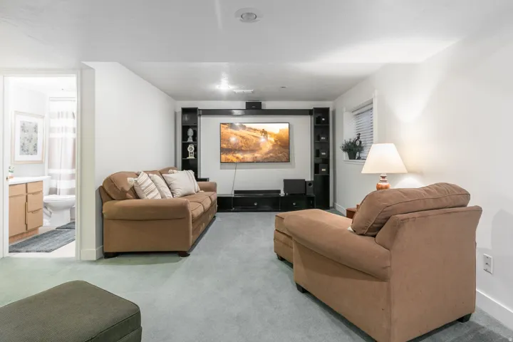 Finished basement recreation room featuring a wall-mounted flat-screen television with built-in media cabinetry, recessed ceiling lighting, neutral carpet flooring, and ample seating arrangements