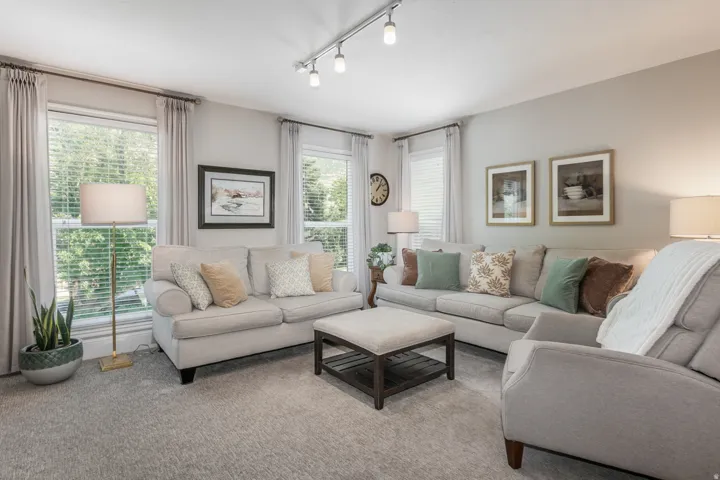 Recessed lighting, light gray wall color, multiple large windows with blinds, and light gray carpeting