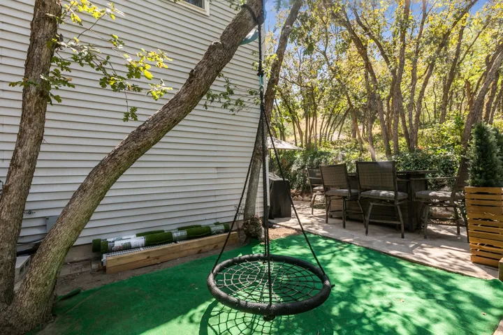 Shaded backyard retreat featuring mature trees, synthetic turf, and a circular swing suspended from established canopy