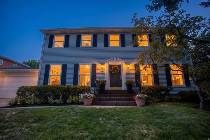 Two-story residence featuring siding exterior, an attached garage, brick steps, and exterior lighting