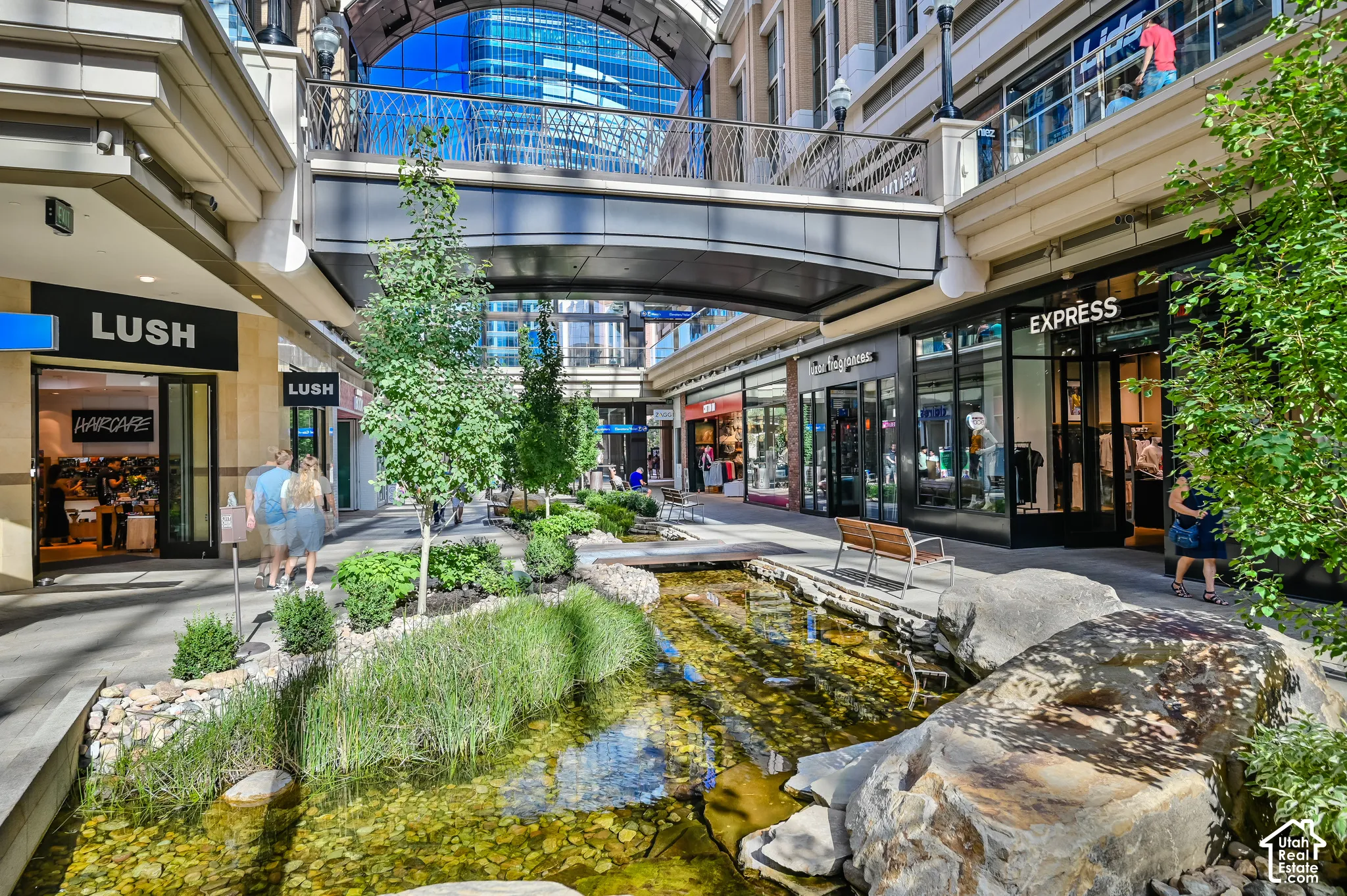 Modern mixed-use atrium featuring a naturalistic water feature with native plantings, decorative stone elements, and integrated landscaping