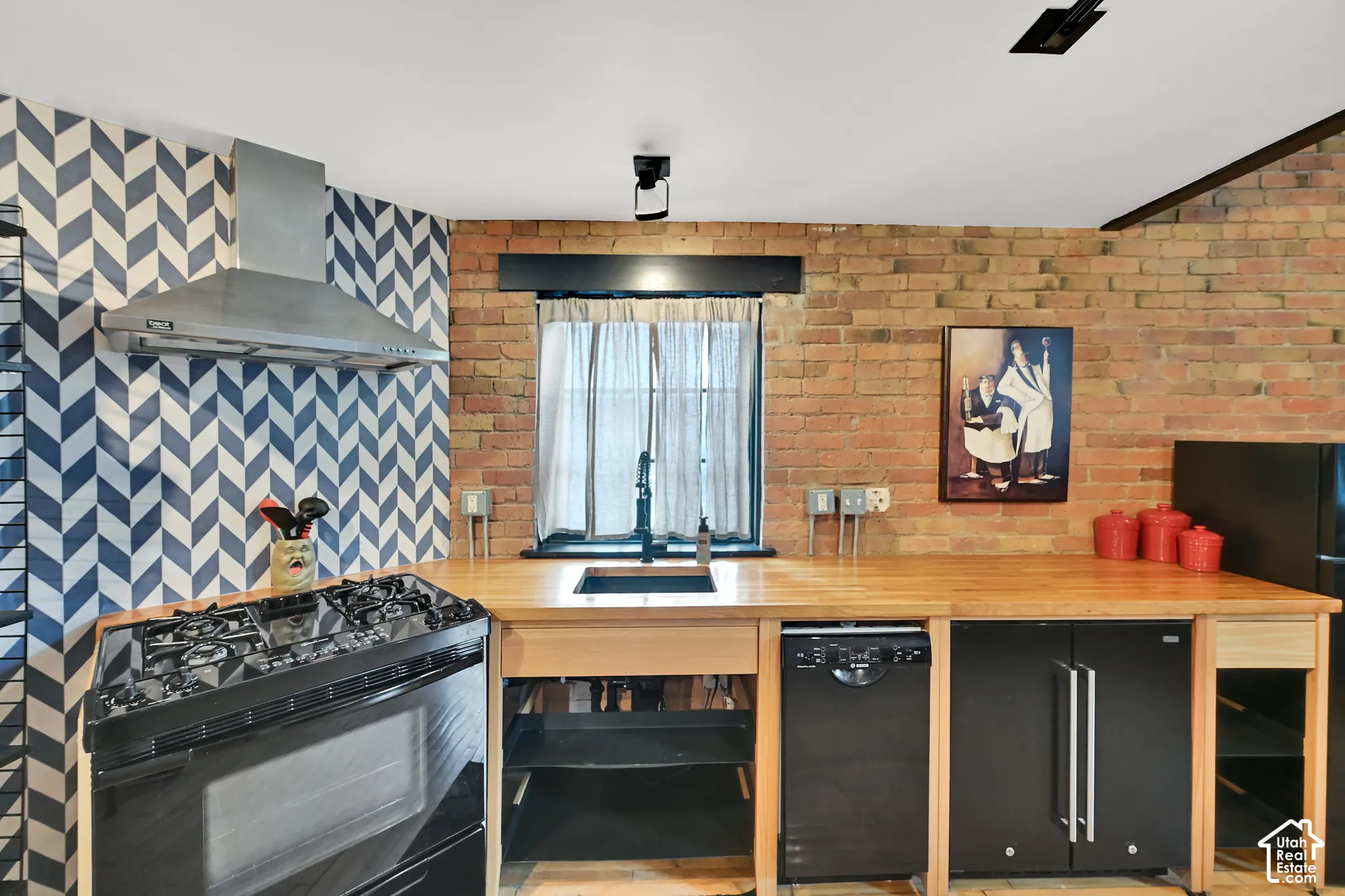 Modern kitchen featuring a wood-finish countertop with open shelving and integrated storage, gas cooktop with stainless steel range hood, and custom cabinetry in natural wood and matte black finishes