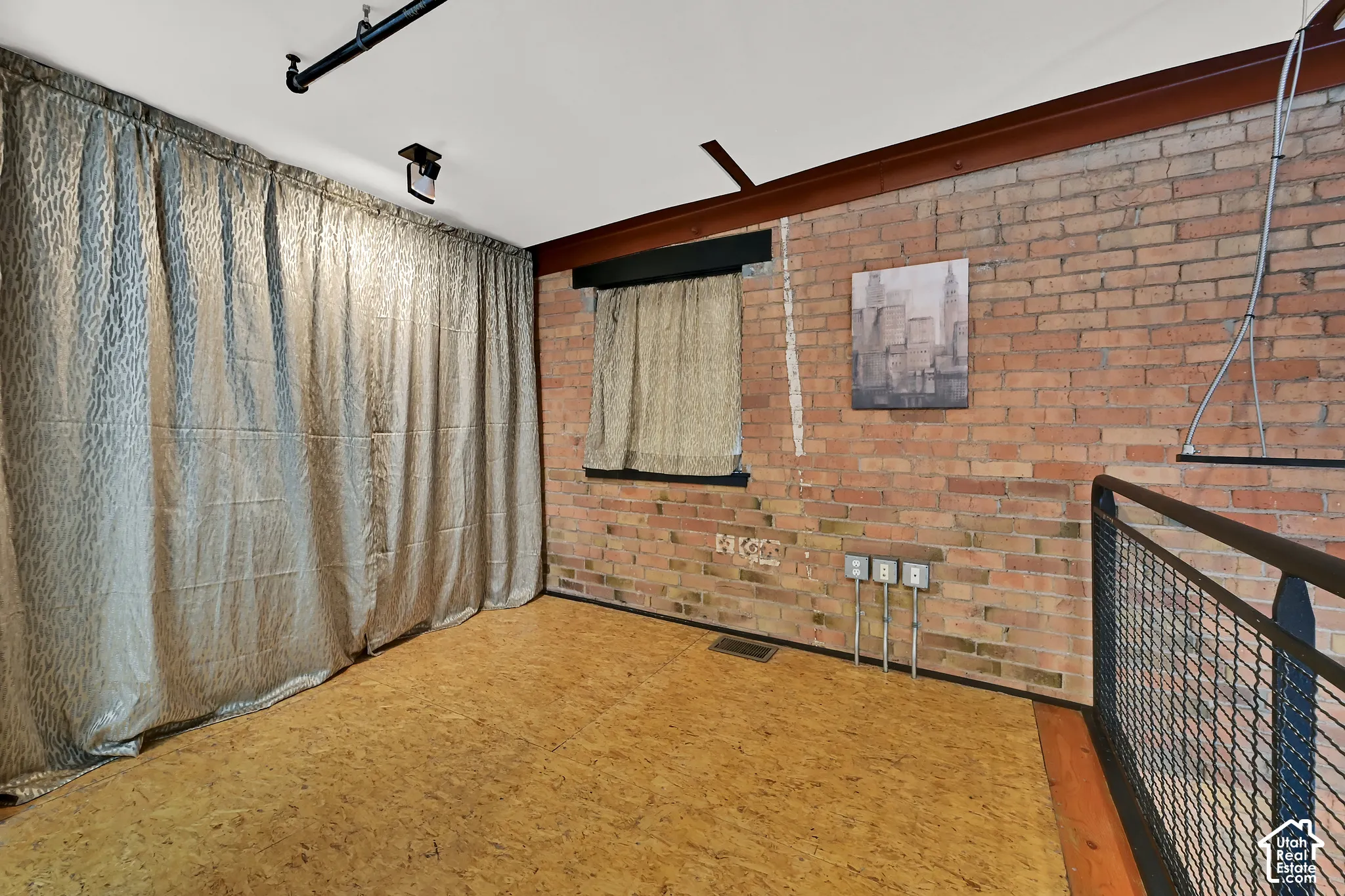 Versatile interior space bedroom & laundry area featuring exposed brick walls, cork wood-finish flooring, and industrial-style ceiling beams