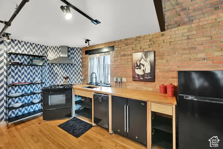 Exposed brick wall, hardwood flooring, stainless steel range hood, track lighting, and butcher block countertops