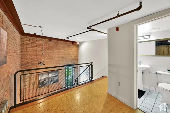 Loft-style mezzanine with exposed brick wall, cork wood-finish flooring, and black metal railing