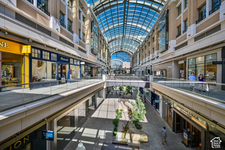 Multi-level retail promenade featuring a vaulted glass ceiling, pedestrian bridges, and structured landscaping
