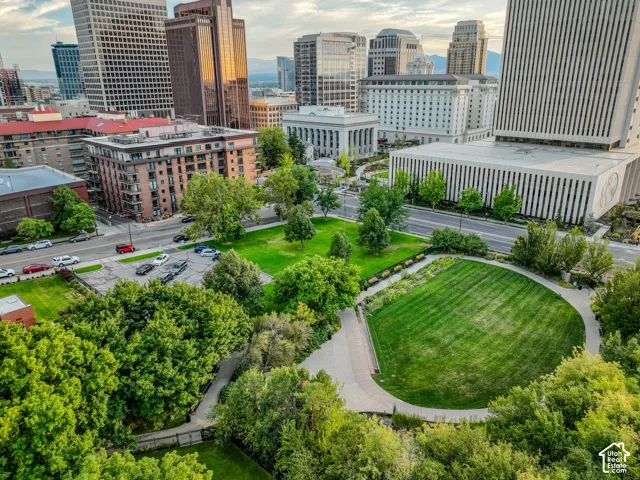 Urban plaza featuring manicured lawns with geometric patterning, mature landscaping throughout, and paved pedestrian pathways