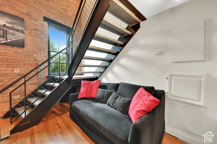 Modern loft featuring exposed brick walls, warm wood-finish flooring, and a contemporary black steel staircase with metal railings